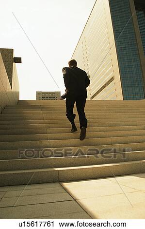 Stock Image - Rear view of a person climbing stairs. Fotosearch