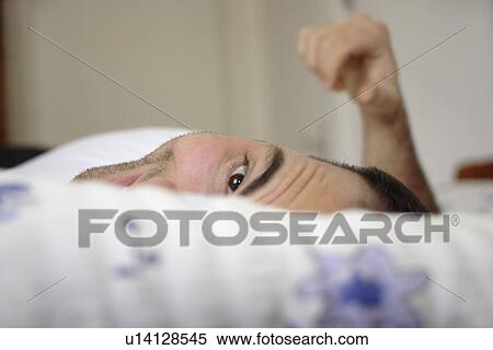 Stock Photography - Young man lying in bed, smiling and relaxing. Fotosearch