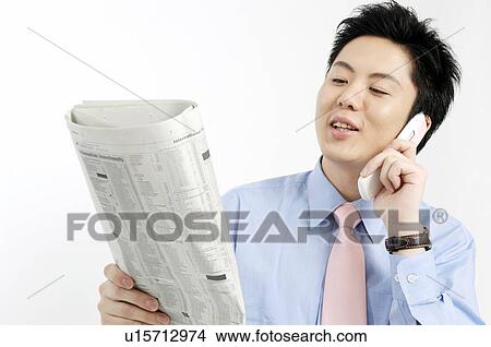 Picture - Businessman calling with cell phone and watching a newspaper. Fotosearch