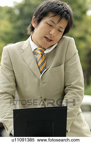 Businessman who watches a PC while talking with the cell phone View Large Photo Image Stock Photography - Businessman who watches a PC while talking with the cell phone. Fotosearch