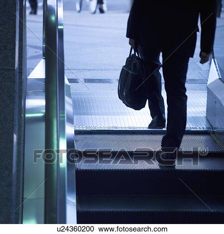 Stock Image - A businessman stepping off of escalator. Fotosearch