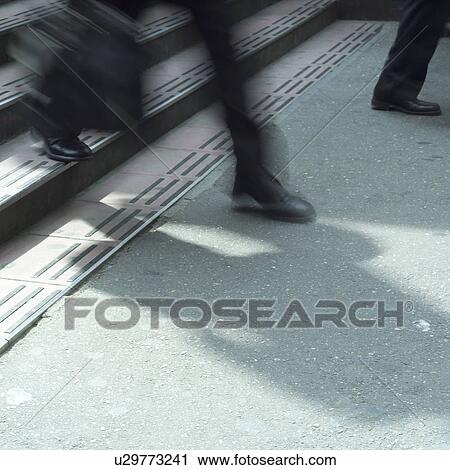 Stock Image - Low section of a businessman descending steps, blurred motion. Fotosearch