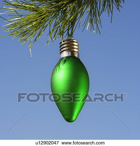 Green ornament hanging on Christmas tree branch against blue background. View Large Photo Image Stock Photo - Green ornament hanging on Christmas tree branch against blue background.. Fotosearch