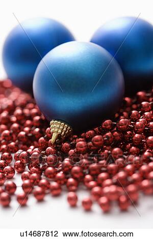 Stock Image - Still life of large blue Christmas ornaments and strings of red beads.. Fotosearch