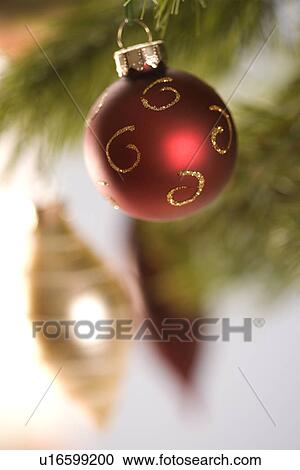 Stock Image - Still life of red and gold Christmas ornaments hanging from pine branch.. Fotosearch