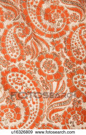 Stock Photo - Close-up of orange textural vintage fabric with paisley and metallic thread stitching. Fotosearch