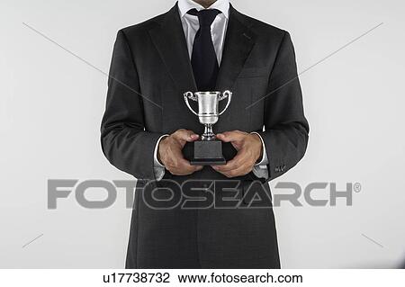 Stock Image - Man holding a small silver trophy.. Fotosearch