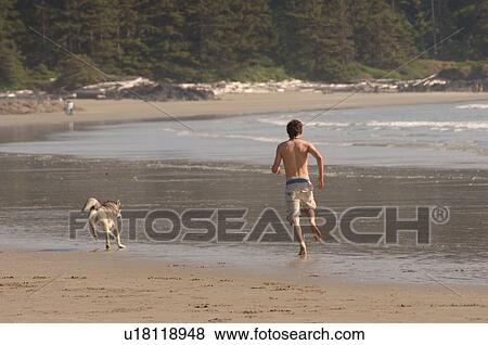 Stock Photo - Man chasing dog on beach. Fotosearch