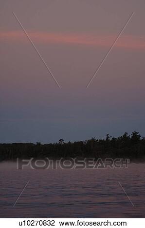 Stock Image - Silhouette of shoreline against twilight sky. Fotosearch