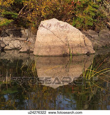 Stock Image - Large rock protruding out of the water. Fotosearch