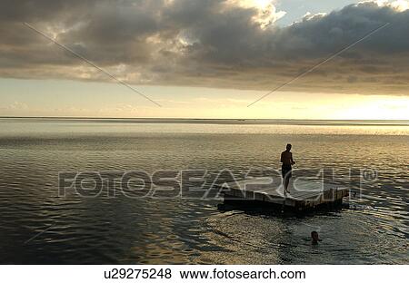 Stock Photo - A man standing on a raft in the sea, Moorea, Tahiti, French Polynesia, South Pacific. Fotosearch