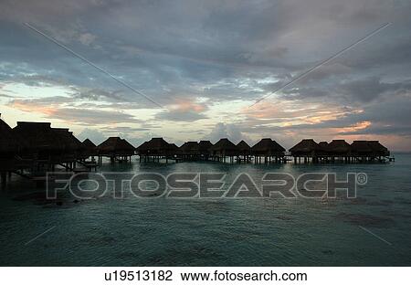 Stock Image - Rows of thatched buildings on stilts in the sea, Moorea, Tahiti, French Polynesia, South Pacific. Fotosearch