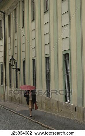 Woman walking holding an umbrella on a sidewalk in Prague View Large Photo Image Stock Image - Woman walking holding an umbrella on a sidewalk in Prague. Fotosearch