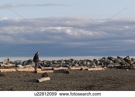 Stock Photo - Man walking amongst logs on shoreline. Fotosearch
