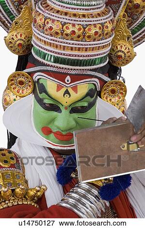 Stock Photo - Close-up of a Kathakali dance performer applying make-up on his face. Fotosearch