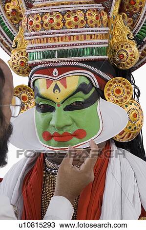Stock Image - Close-up of a man applying make-up on face of a Kathakali dance performer. Fotosearch