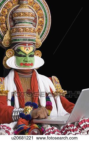 Stock Image - Portrait of a Kathakali dance performer using a laptop. Fotosearch