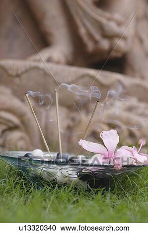 Stock Image - Close-up of burning incense sticks with pebbles in a glass bowl. Fotosearch