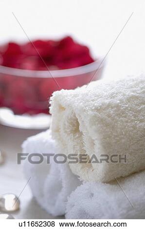 Stock Photo - Close-up of rose petals in a bowl with three rolled white towels. Fotosearch