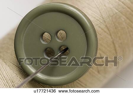 Stock Photograph - Close-up of a green button and a needle with a spool of thread. Fotosearch