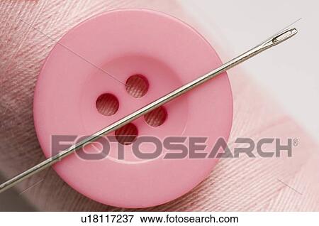 Stock Photo - Close-up of a pink button and a needle with a spool of pink thread. Fotosearch