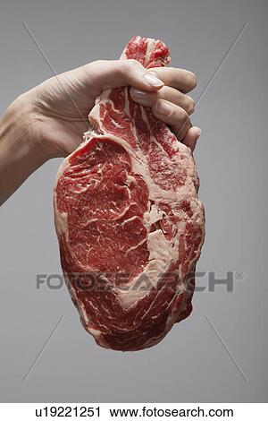 Stock Image - Woman's hand holding raw steak (close-up). Fotosearch