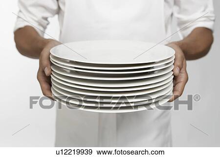 Stock Photo - Chef holding stack of dinner plates (mid section). Fotosearch
