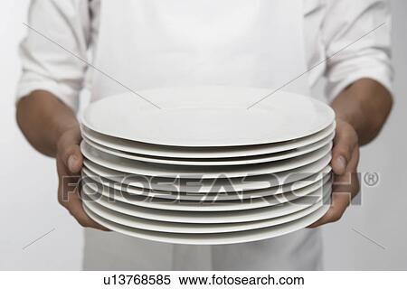 Stock Photography - Chef holding stack of dinner plates (mid section). Fotosearch