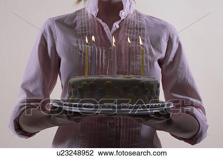 Stock Image - Woman carrying birthday cake (close-up, midsection). Fotosearch