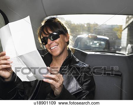 Stock Photo - Woman reading a letter in a car, smiling. Fotosearch