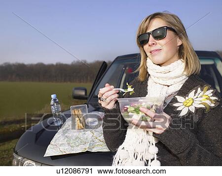 Stock Image - Young woman having lunch at rest stop. Fotosearch