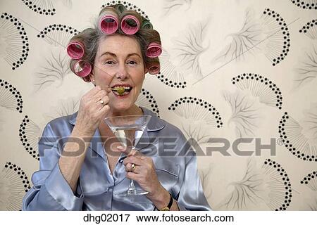 Senior Woman Eating Olive From Martini With Hair In Curlers Stock Photo