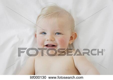 Portrait Of Smiling Blue Eyed Baby Boy With Blond Hair Lying On A