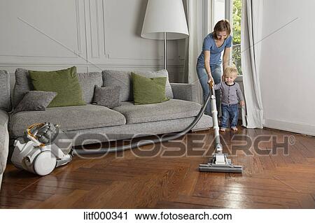 Laughing Toddler Helping His Mother Hoovering Wooden Floor Stock