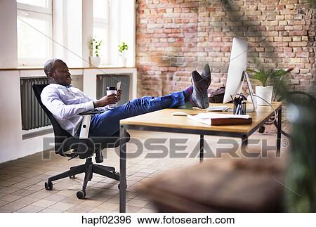 Businessman Sitting In Office With Feet On Desk Checking Cell