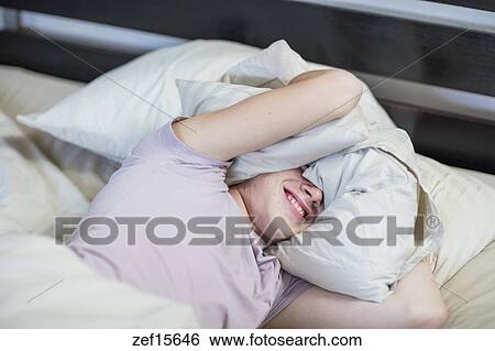 Boy Lying In Bed Holding Pillow Over His Head Stock Photograph