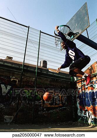 Man hanging on basketball rim after dunking ball View Large Photo Image Stock Photo - Man hanging on basketball rim after dunking ball. Fotosearch