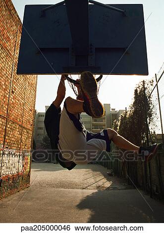 Man hanging on basketball rim after dunking ball, shot from behind View Large Photo Image Stock Photograph - Man hanging on basketball rim after dunking ball, shot from behind. Fotosearch
