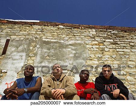 Men sitting sie by side in urban setting, low angle view View Large Photo Image Stock Photo - Men sitting sie by side in urban setting, low angle view. Fotosearch