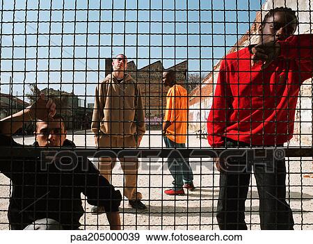 Men standing behind fence in urban playground View Large Photo Image Stock Photo - Men standing behind fence in urban playground. Fotosearch
