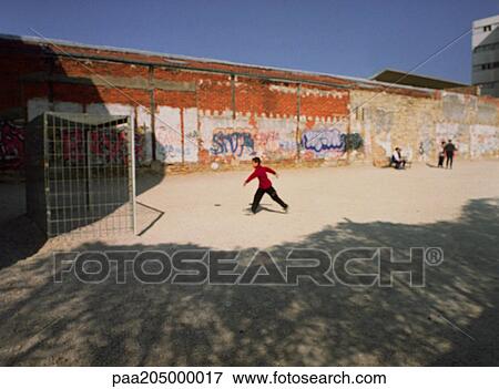 Stock Photo - Person playing soccer on dirt yard next to graffiti wall. Fotosearch
