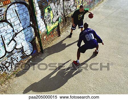Two men playing basketball in front of graffitied wall in urban playground View Large Photo Image Stock Photography - Two men playing basketball in front of graffitied wall in urban playground. Fotosearch
