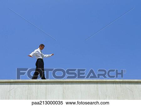 Businessman walking on edge of building, low angle view View Large Photo Image Stock Photography - Businessman walking on edge of building, low angle view. Fotosearch