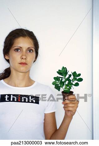 Stock Image - Portrait of woman holding small potted plant up with hand. Fotosearch