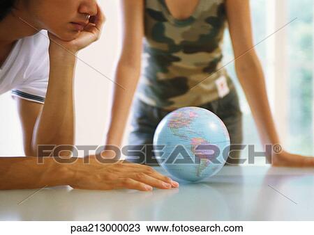 Stock Image - Two people looking at globe on table. Fotosearch