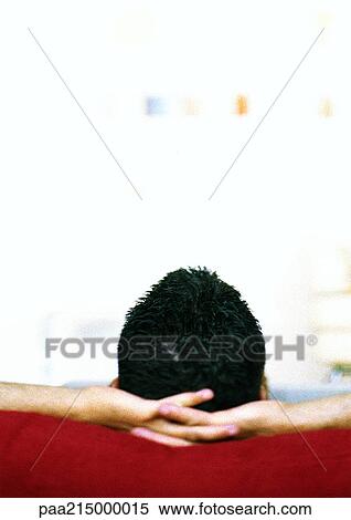 Stock Photography - Man sitting with hands behind head, rear view.. Fotosearch