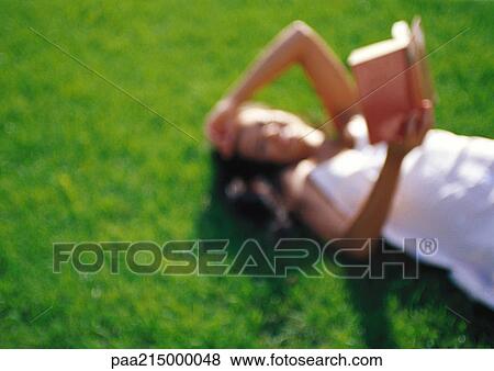 Woman lying on grass, reading, defocused View Large Photo Image Stock Photo - Woman lying on grass, reading, defocused. Fotosearch