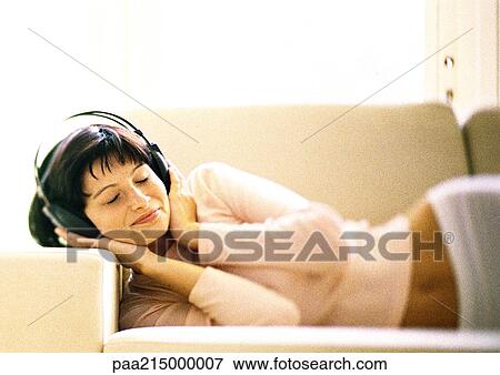 Woman lying on sofa, listening to headphones. View Large Photo Image Stock Photo - Woman lying on sofa, listening to headphones.. Fotosearch