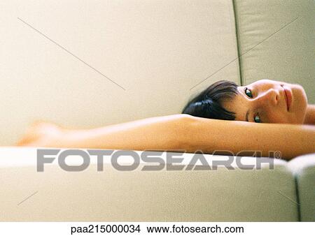 Woman lying on sofa with arms above head, looking at camera View Large Photo Image Picture - Woman lying on sofa with arms above head, looking at camera. Fotosearch