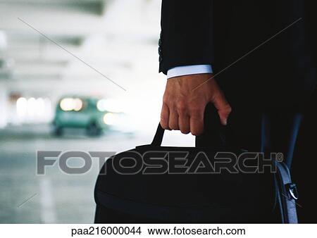 Businessman holding briefcase in parking garage, blurred, close-up. View Large Photo Image Picture - Businessman holding briefcase in parking garage, blurred, close-up.. Fotosearch